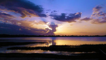 Purple Majesty - A golden sunset  fills the sky with blue, purple, yellow, orange and gold colors as the sun sets over a calm and peaceful lake surrounded by beaches, sand and wet marshland for birds siignifying the end of another day.  Just like an Easter Sunrise, a sunset can be a powerful reminder of who put the lights in the sky and calms the water and who is in control of and the author of every living thing bowing in majesty to the Creator of all the Heavens and the Earth, Jesus Christ. 