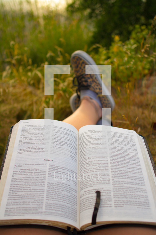 feet of a man reading a Bible outdoors 