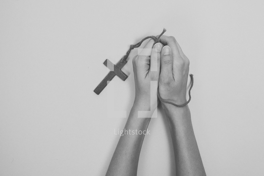 praying hands holding a cross necklace 