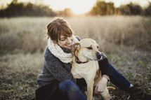 Smiling woman witting with her dog in a field.