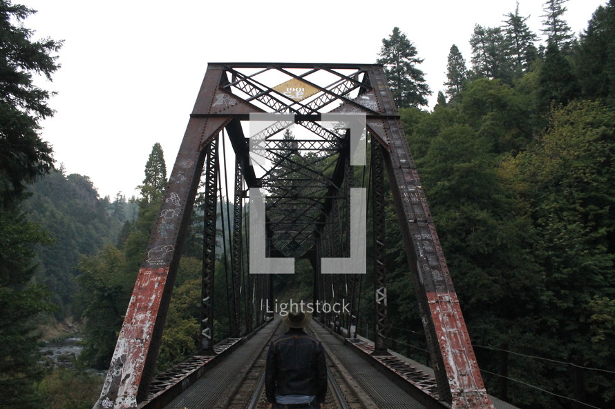 Back of a man walking on a train track on a bridge.