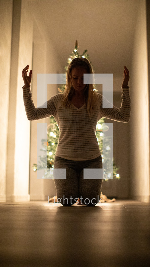 a woman kneeling in prayer in front of a Christmas tree 