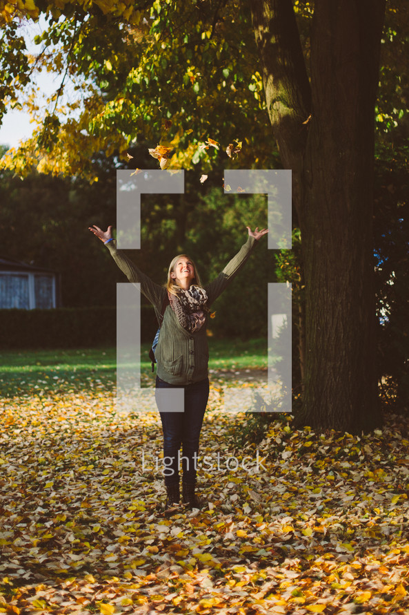 woman standing in fall leaves with her arms raised 