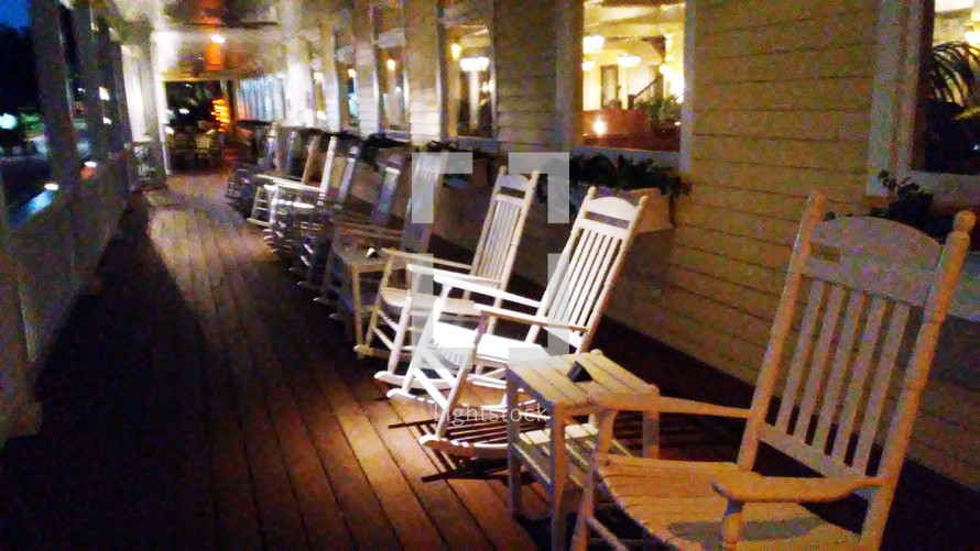A row of white wooden rocking chairs line a front porch of a local historic inn for summer vacations, retirees and summer renters looking for a restful relaxing vacation. 
