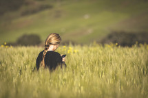 a woman standing in a field of tall grasses holding a cellphone 