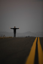 man with outstretched arms standing on a road 