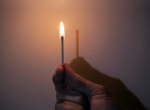 hand holding a match, flame has no shadow, "I am the light"