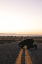 a man kneeling in prayer on the center lines of a road 