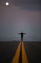 a man standing in the middle of a road with outstretched arms 