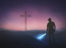 man holding a flashlight at night and a cross