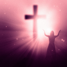 woman standing in front of a glowing cross with her hands raised in worship and praise