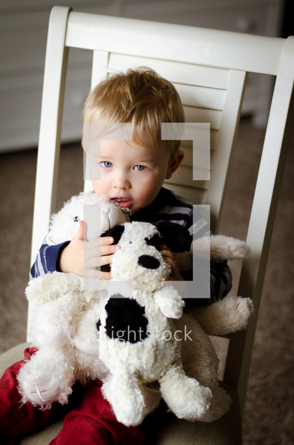 a toddler boy sitting in a chair hugging stuffed animals 