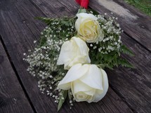 A bouquet of white roses surrounded by babies breathe draped over an old wooden bench for a special wedding day, valentines day or any celebration of love between  a man and a woman. 