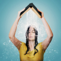 A woman holding an open Bible above her head as water pours on her. 