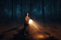 a woman in the woods at night using a Bible as her flashlight 