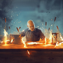 A man is at his desk deep in study with many arrows flying towards him.