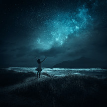 A woman stands with her arms raised toward the Milky Way.