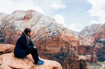 a woman sitting and looking out over red rock mountain peaks