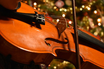 playing a violin in front of a Christmas tree