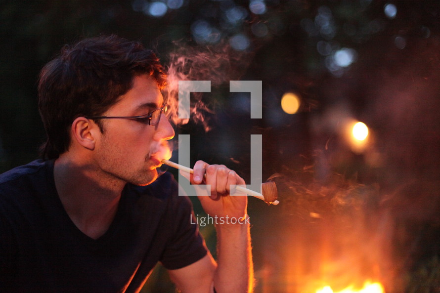 man smoking a pipe by a fire 