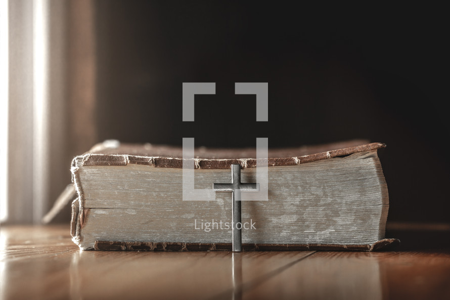 silver cross leaning against a Bible spine 