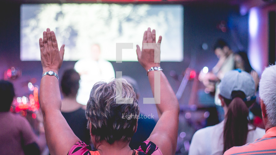 worship leaders singing on stage and woman with raised hands 