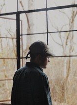 a man in a ball cap looking out a window 