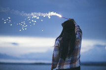A woman holding a fiery sparkler against the evening sky.