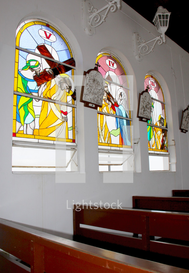 Stained glass church windows and wooden church pews.