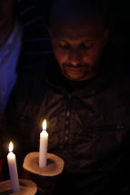 man with bowed head holding a candle 