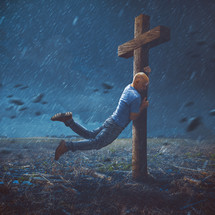 A man clings to a large wooden cross during a heavy storm