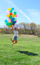 girl jumping up holding helium balloons 