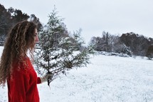 a woman standing in snow holding a pine branch
