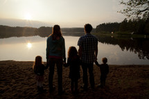 a young family holding hands on a lake shore at fall 
