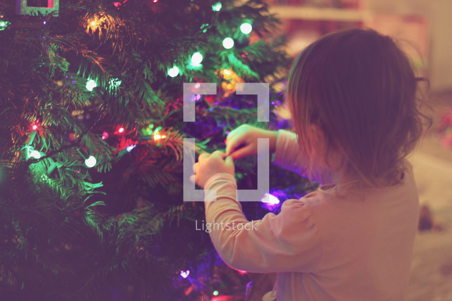 a toddler girl decorating a Christmas tree 