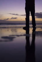 man's legs standing on a beach 