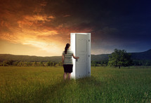 a woman opening a door in a field at sunset