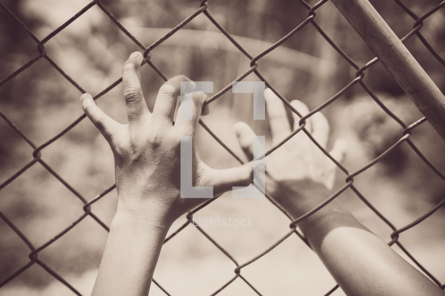 hands grasping to a chain link fence 