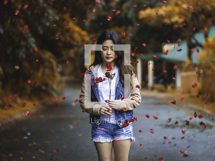 a young woman holding a red rose surrounded by falling rose petals 