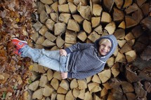 child in front of a stack of fire wood 