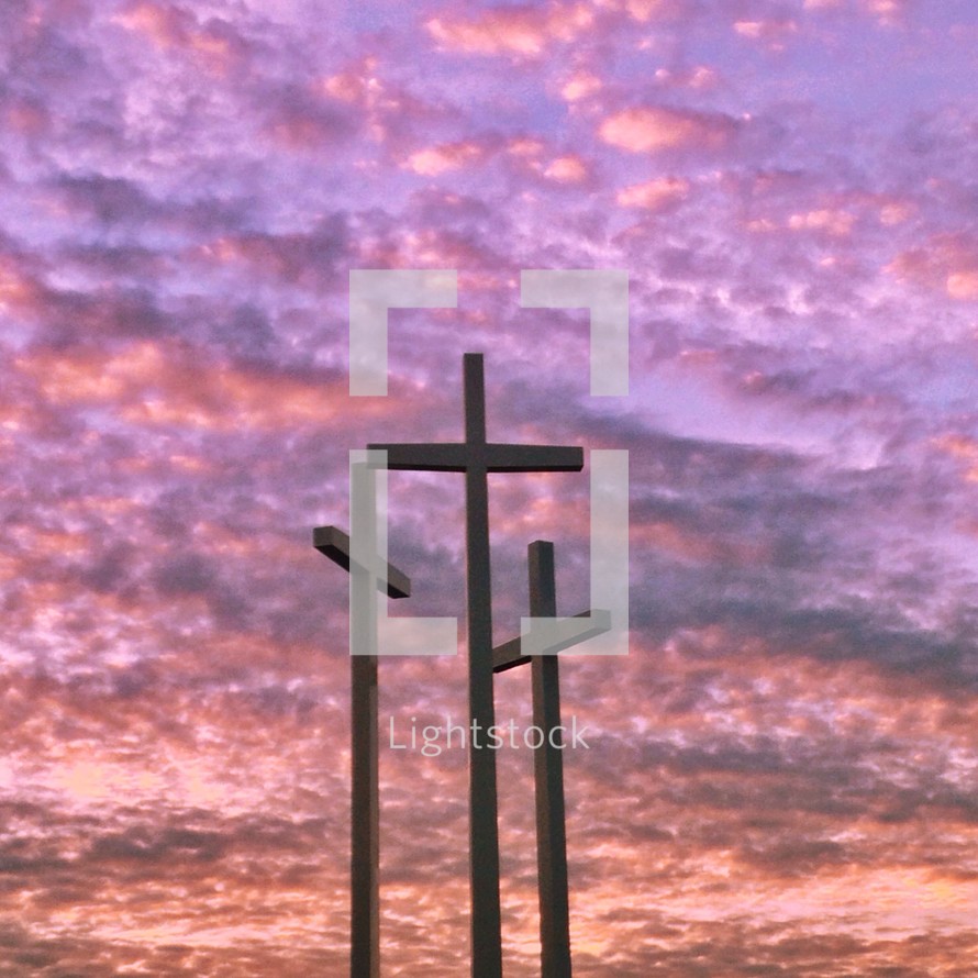 Three crosses under a purple cloudy sky.