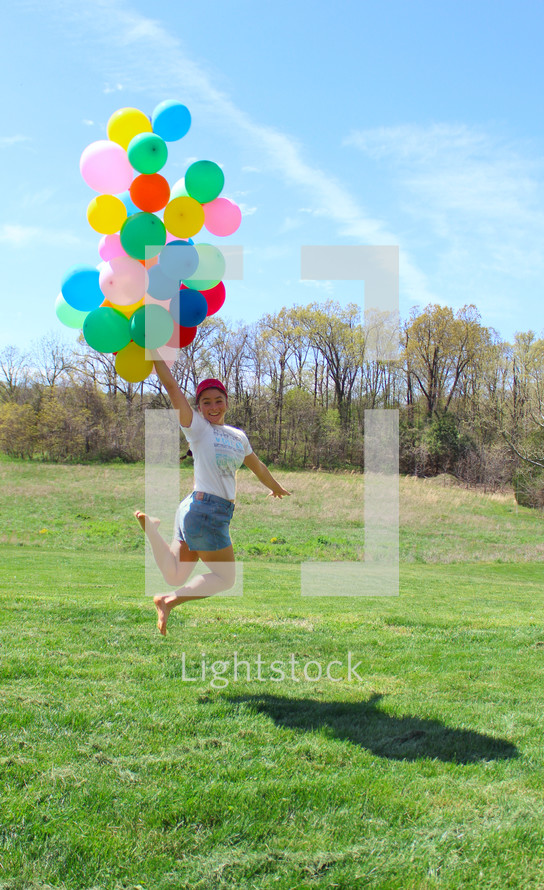girl jumping up holding helium balloons 