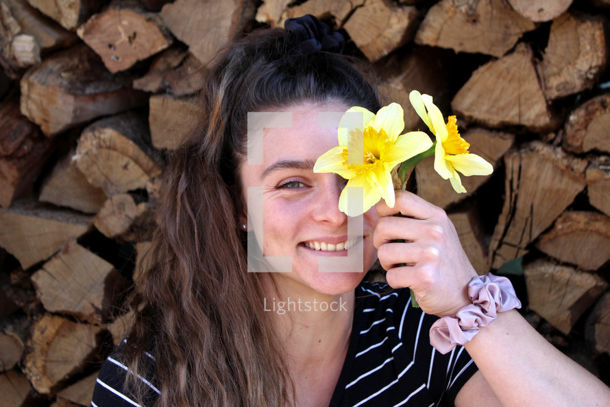 woman holding daffodils in front of a wood pile 
