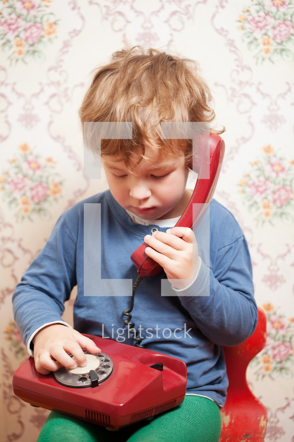 Small boy talking on a red telephone
