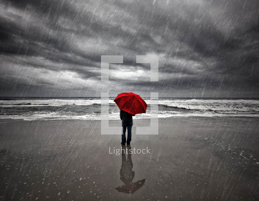 man with a red umbrella standing on a beach in the rain 