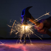 A hammer strikes a nail with bright sparks and fire.