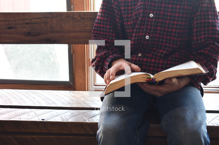 a man sitting in front of a window reading a Bible 