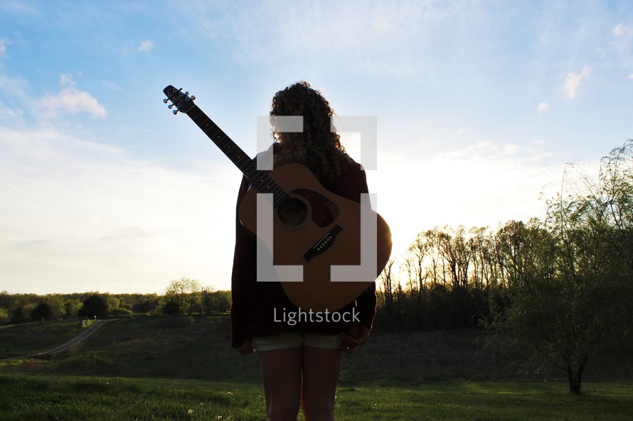 a girl standing outdoors with a guitar on her back 