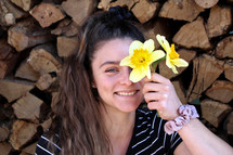 woman holding daffodils in front of a wood pile 