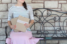 a woman sitting on a bench holding envelopes 